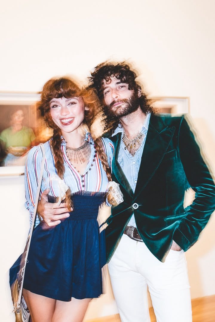 Two guests in the gallery during the opening reception, framed work behind them